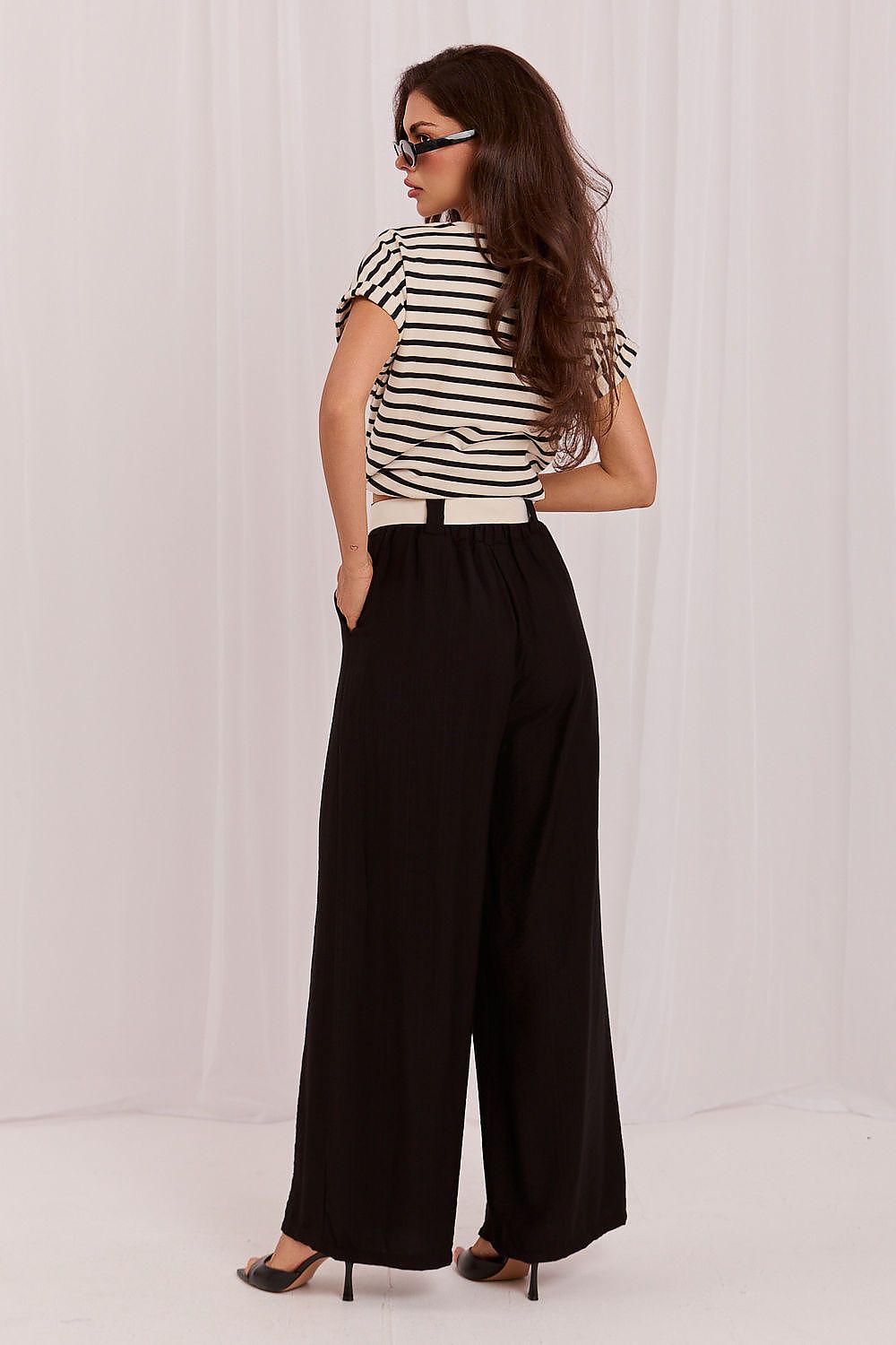 Woman wearing a striped shirt and black wide-leg pants against a white background