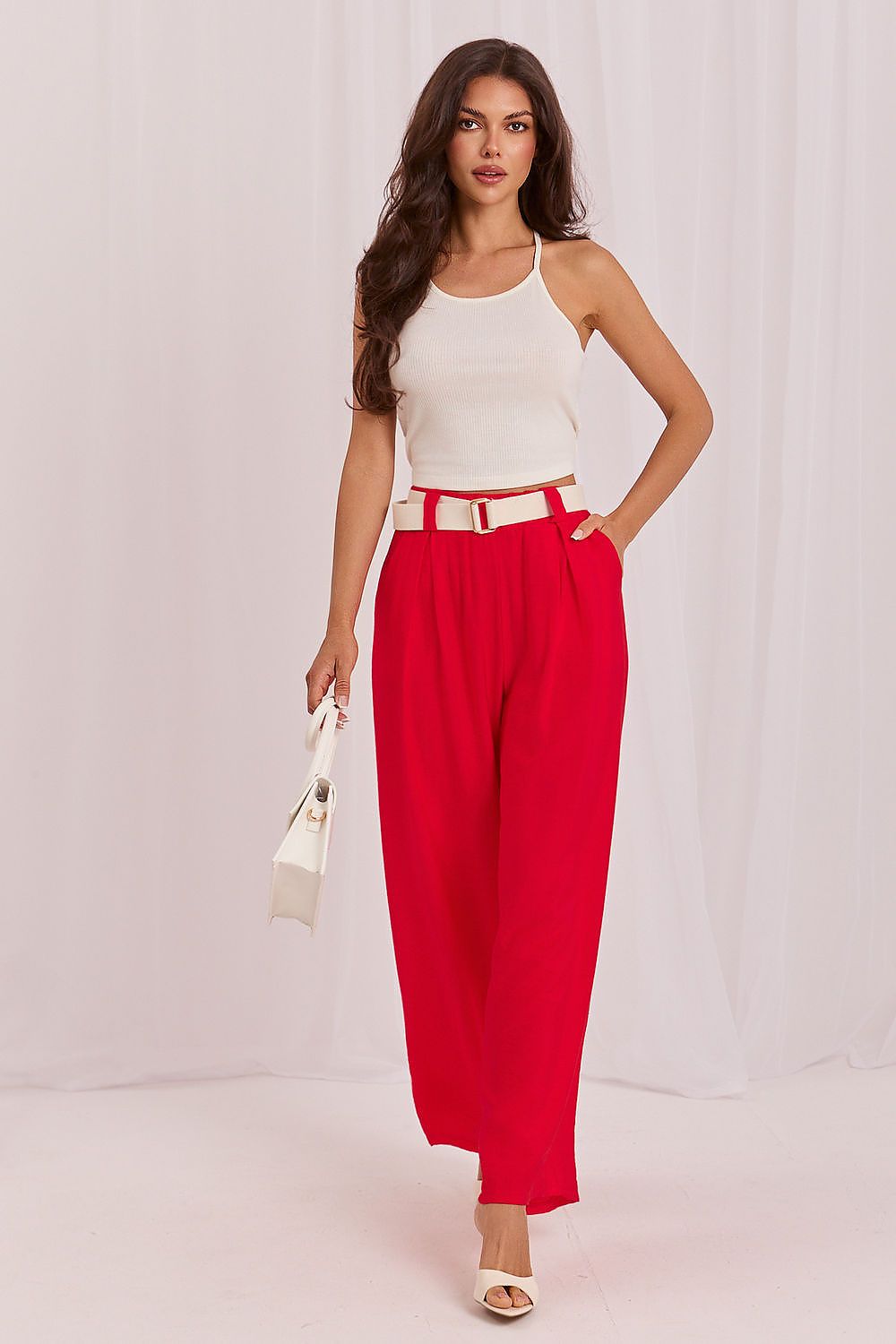 Woman wearing a white top and red pants against a plain background