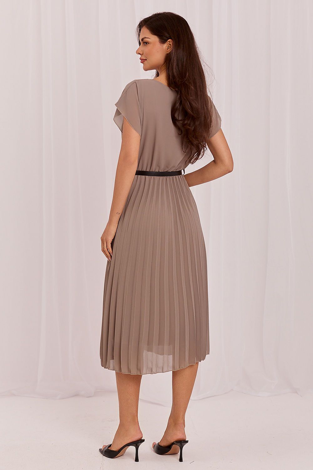 Woman wearing a brown pleated dress against a white background