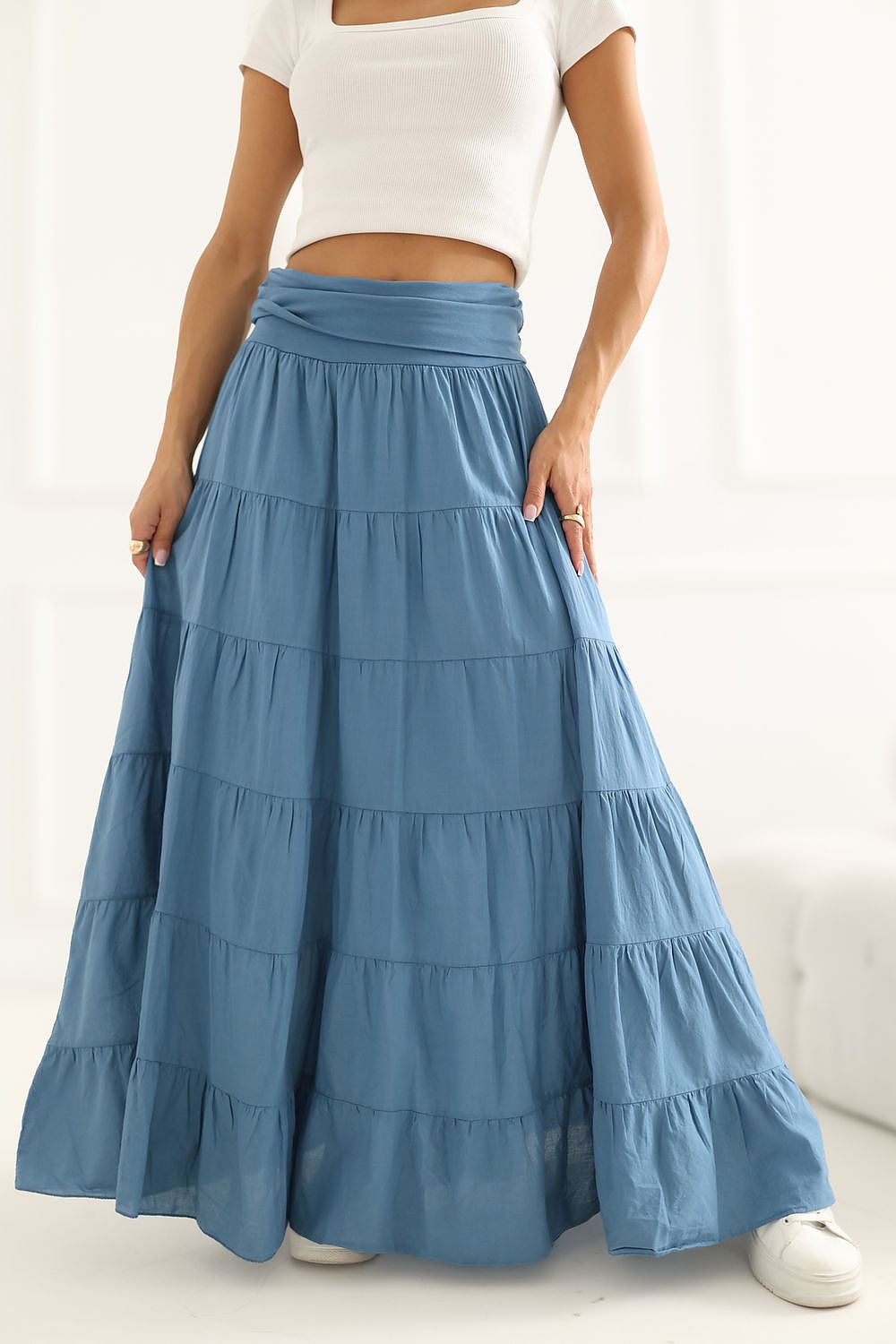 Woman wearing a blue tiered skirt with a white top on a plain background