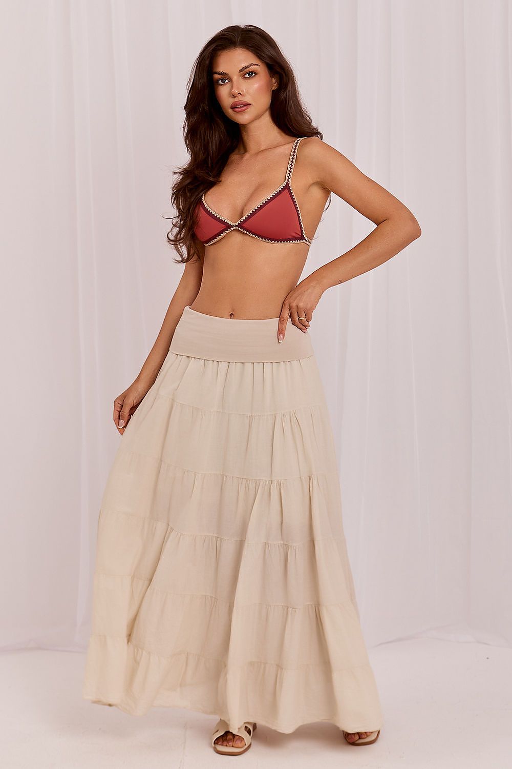 Woman wearing a red bikini top and beige skirt against a white background