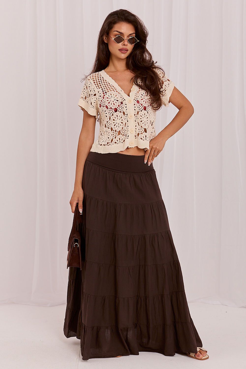 Woman wearing a beige lace top and brown tiered skirt against a white background