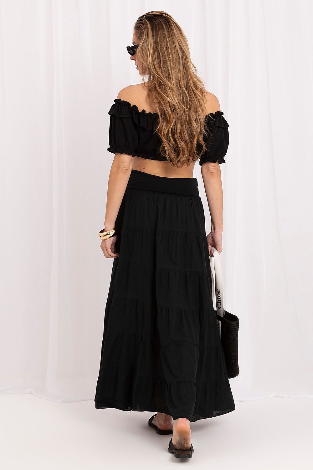 Woman wearing a black off-shoulder top and long skirt against a white background