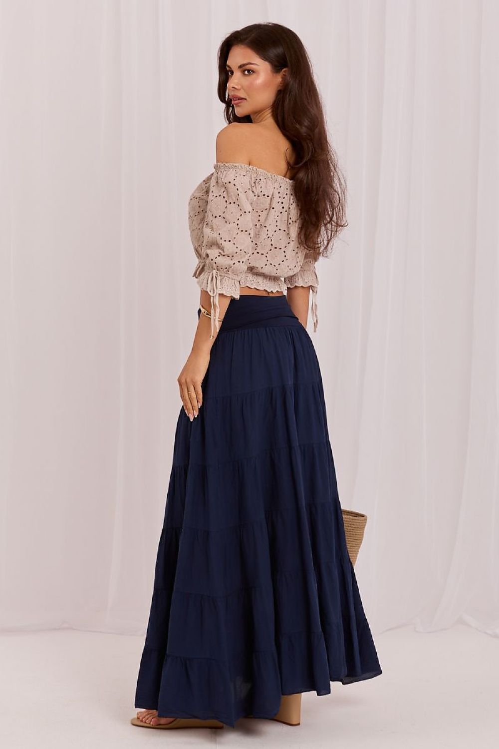 Woman wearing a beige top and navy blue skirt against a white background