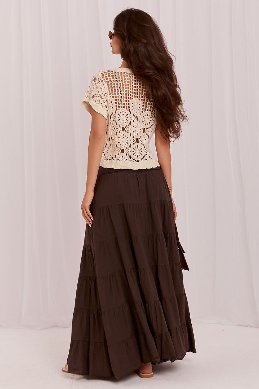 Woman wearing a white lace top and brown tiered skirt against a white background