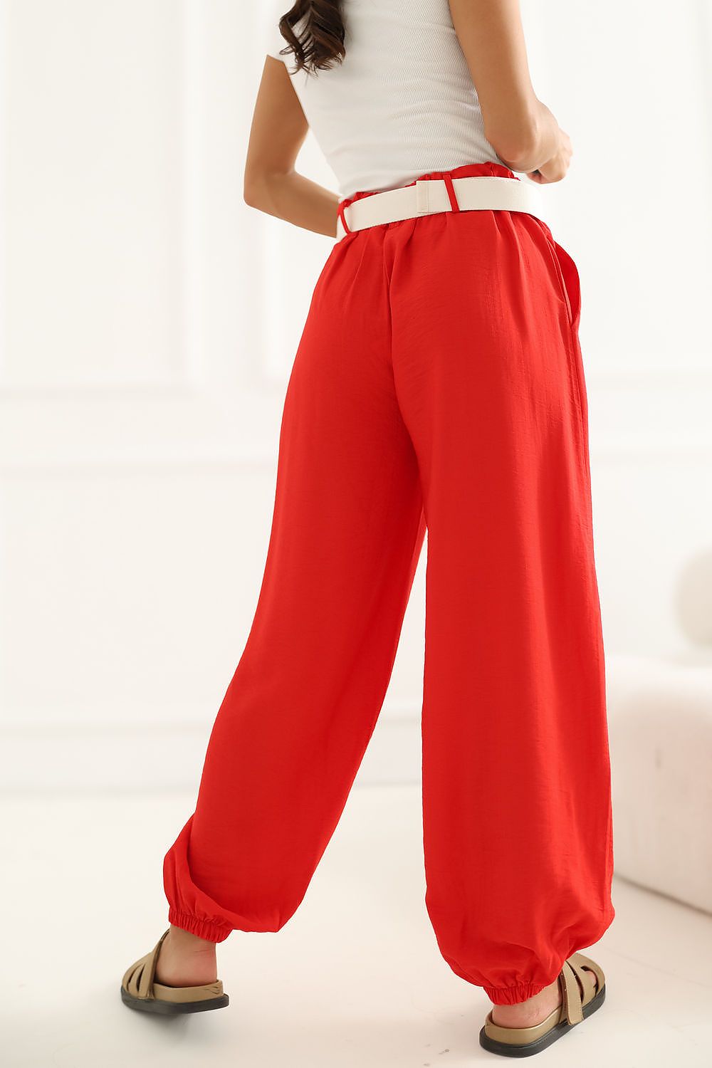 A person wearing bright red wide-leg pants with a white belt, shown from the back in a clean indoor setting.