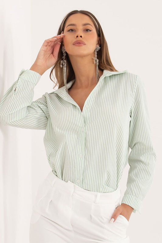 A woman wearing a light sage green and white vertically striped button-up shirt with white trousers, accessorized with long silver dangle earrings, against a clean white background.