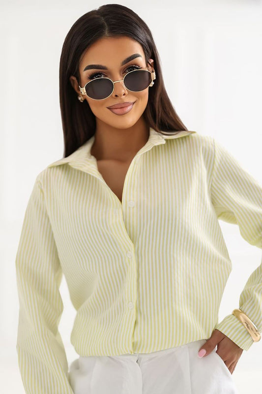 A woman wearing a pale yellow-green vertically striped button-up shirt and white pants, styled with round sunglasses, against a clean white background.