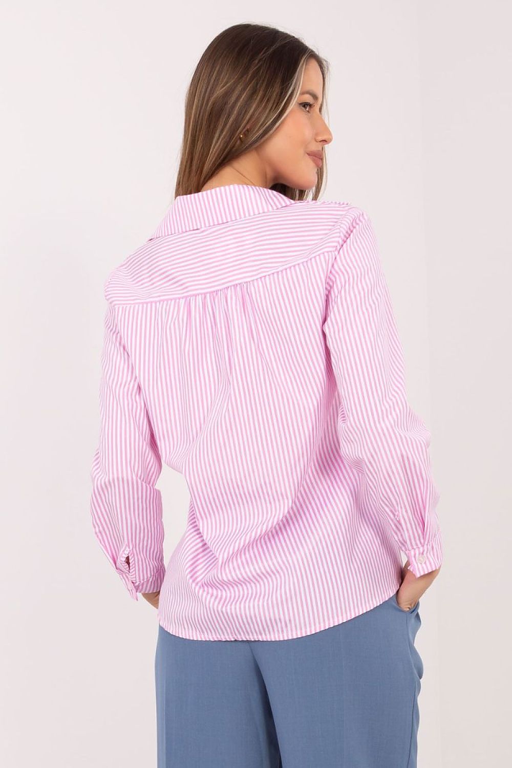 A woman shown from the back wearing a pink and white vertically striped long-sleeve blouse with a wide collar, paired with blue pants, against a plain light background.