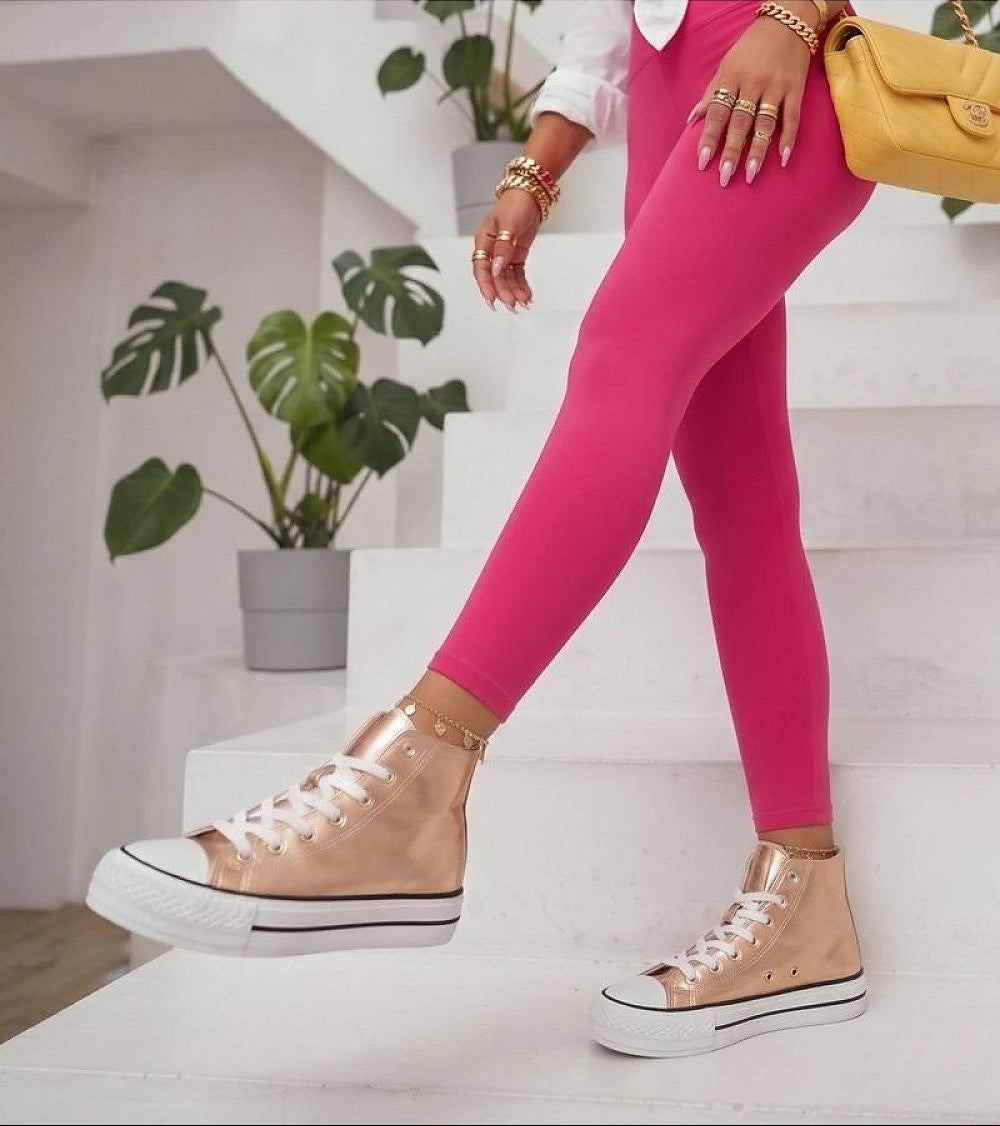 A person wearing bright pink leggings and metallic rose gold high-top sneakers, standing on white stairs with a yellow handbag and potted plants in the background.