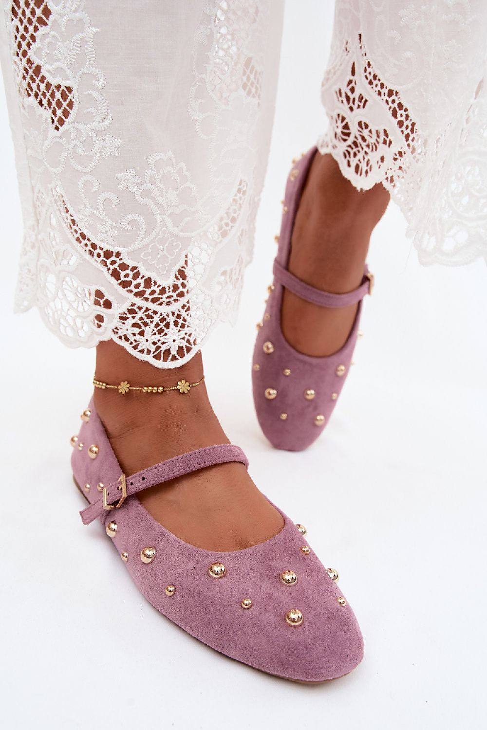 A pair of mauve suede Mary Jane shoes with gold-tone studs, shown on a model's feet with white lace-trimmed pants visible at the top.