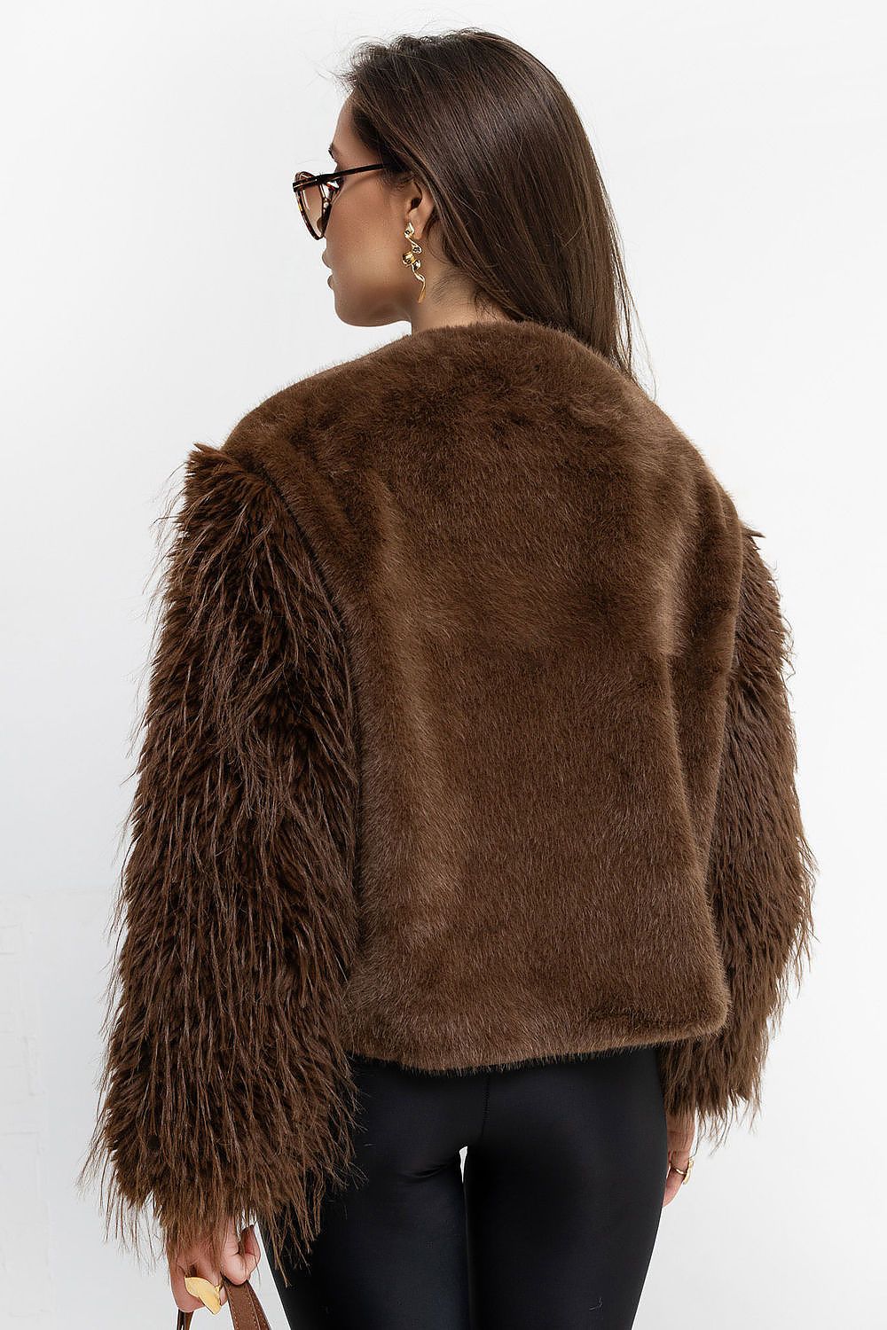 A woman shown from the back wearing a brown faux fur jacket with shaggy long sleeves, paired with black pants, against a plain white background.
