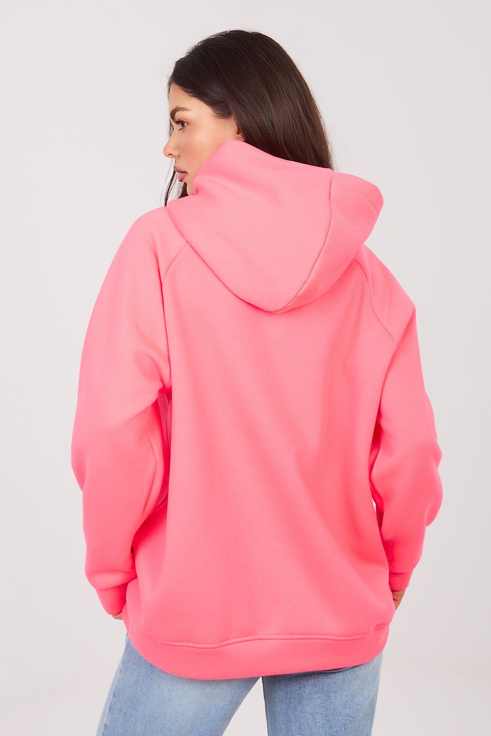 A woman shown from the back wearing a bright pink pullover hoodie and light blue jeans against a plain light gray studio background.