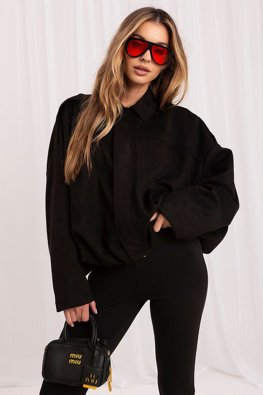 A woman wearing a black oversized collared shirt, black pants, red-tinted sunglasses, and holding a black Miu Miu handbag against a white draped background.