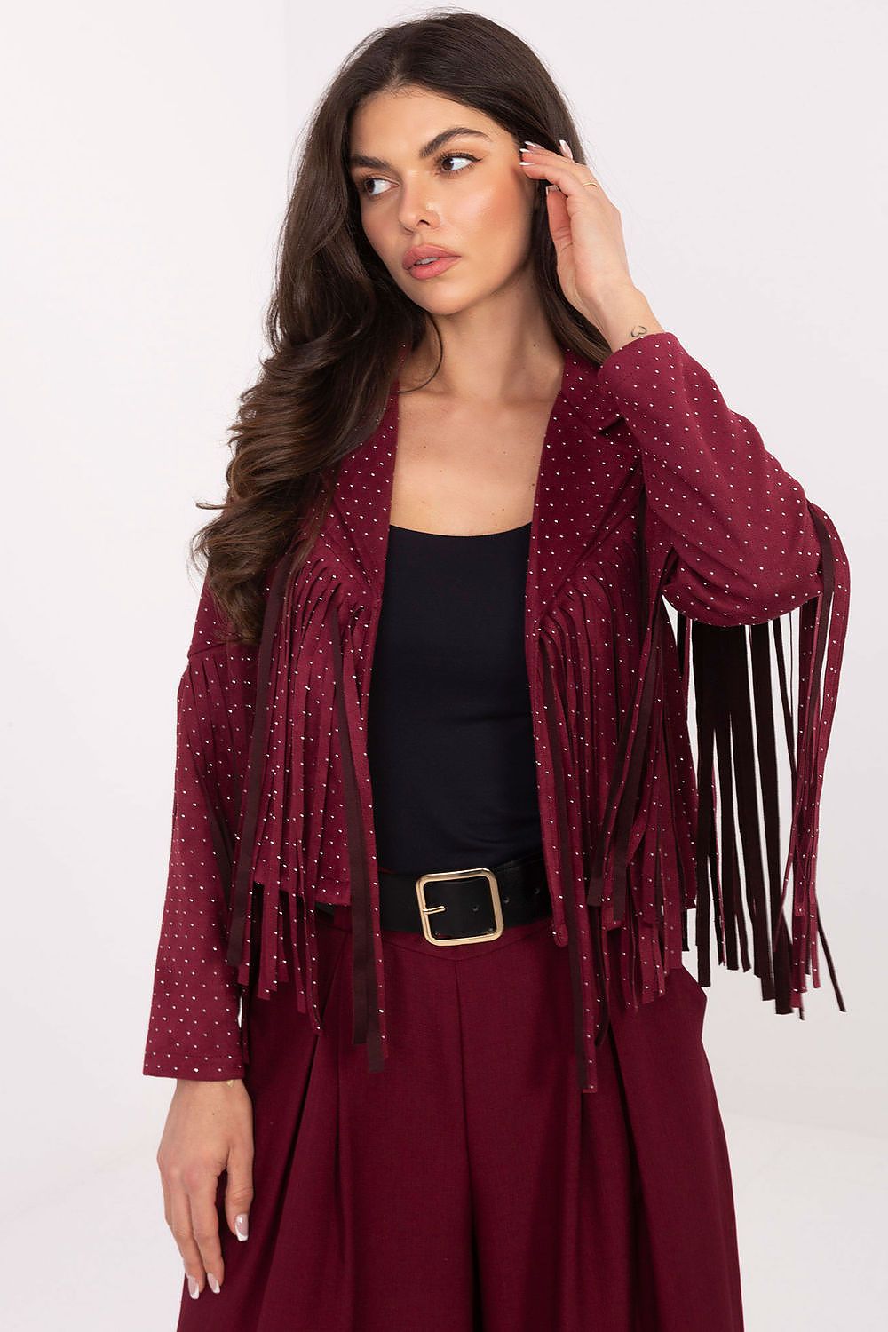 A woman models a burgundy fringed jacket with small white polka dots, worn over a black top and matching burgundy pants against a plain white studio background.