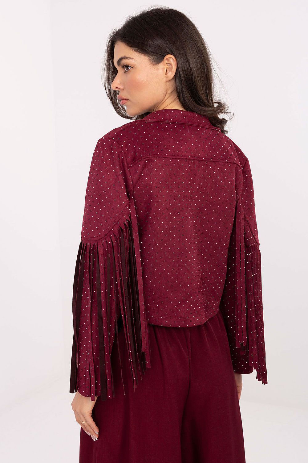 A woman shown from the back wearing a burgundy fringed jacket with a subtle polka dot pattern and matching burgundy pants, set against a plain white studio background.