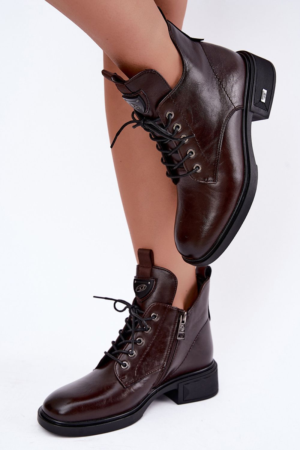 A pair of dark brown leather lace-up ankle boots with black soles, shown on a model's feet against a plain white background.