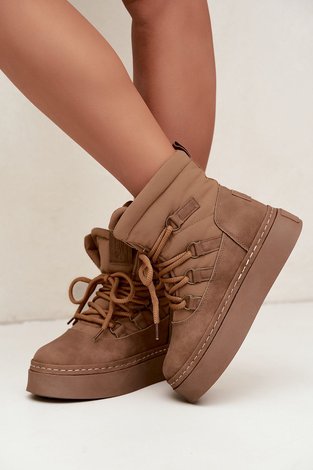 A pair of mid-calf platform ankle boots in a warm taupe-brown suede-like material, shown worn on a model's feet against a clean off-white studio background.
