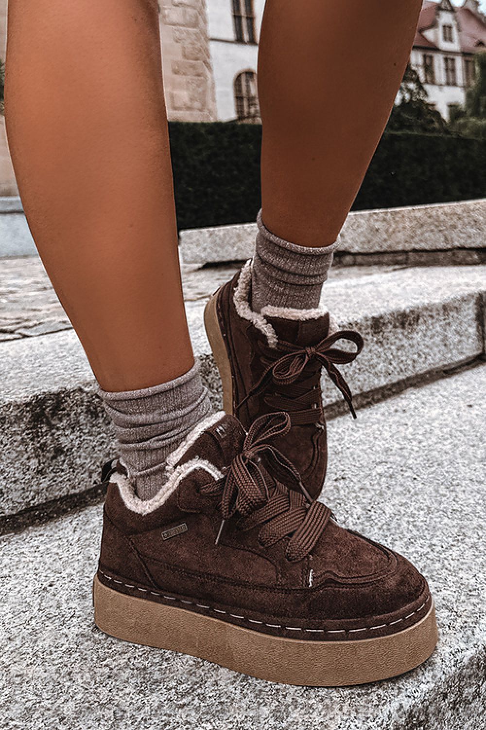 A person wearing dark brown suede platform sneakers with white sherpa lining and gray socks, standing on outdoor stone steps.