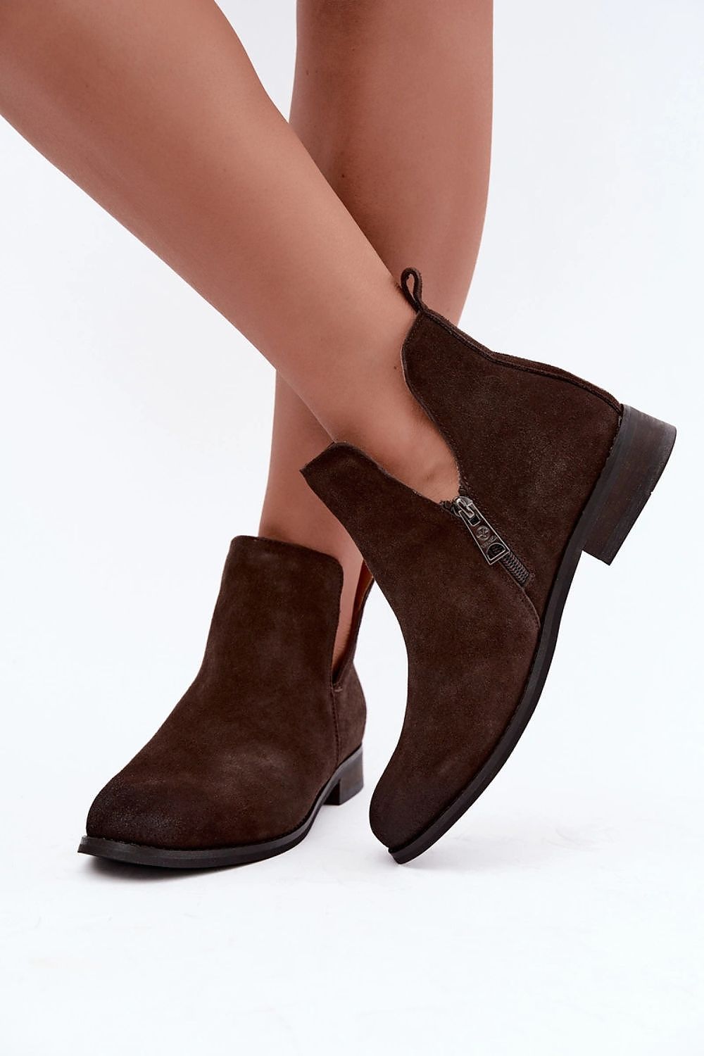 A pair of dark brown suede ankle boots with side zippers, shown on a model's feet against a plain white background.