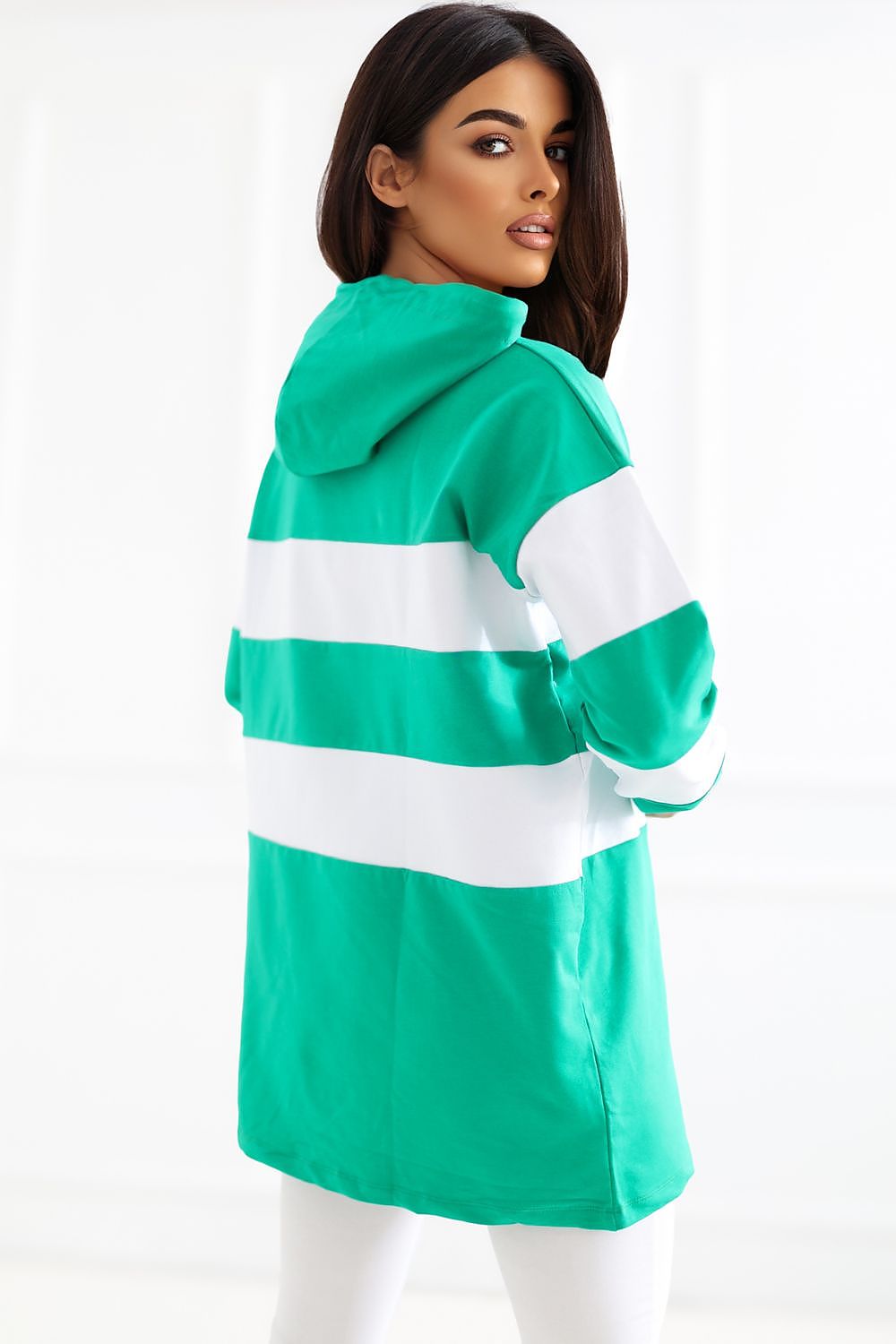 A woman wearing a bright green hooded sweatshirt with bold white horizontal stripes, shown from the back against a clean white studio background.