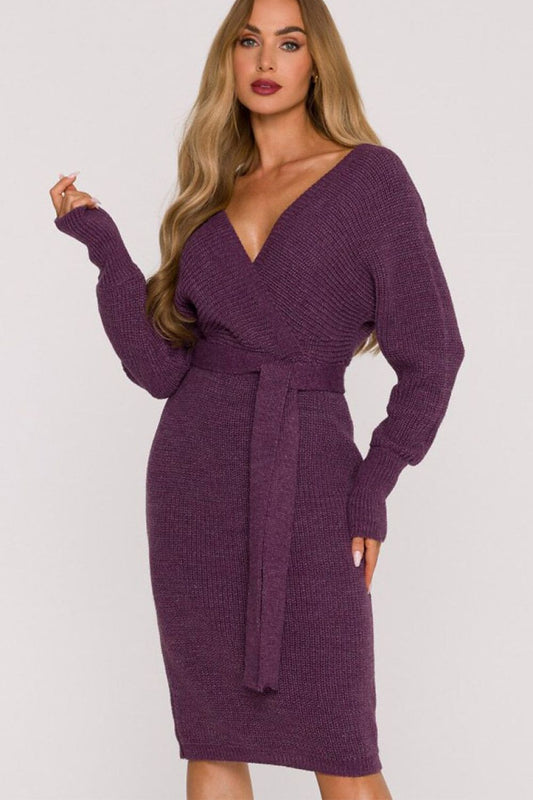 A woman modeling a ribbed knit long-sleeve bodycon dress in a deep plum purple color, featuring a wrap-style V-neckline with a matching tie belt at the waist.
