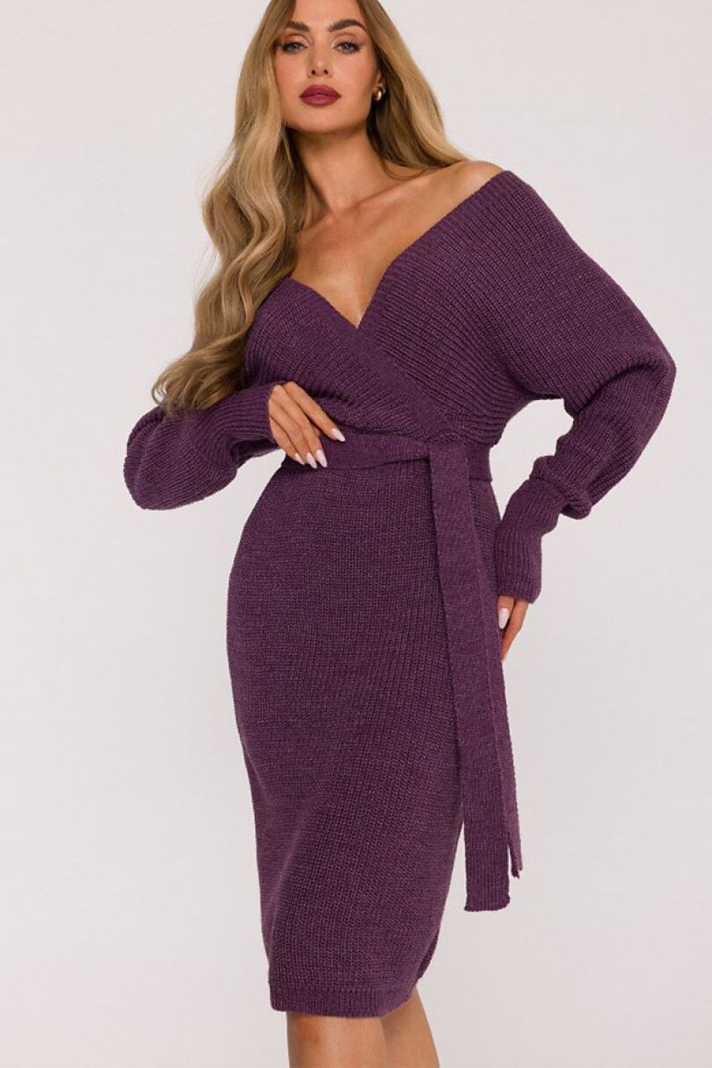 A woman modeling a ribbed knit off-the-shoulder wrap dress in a deep purple color, set against a plain light gray background.