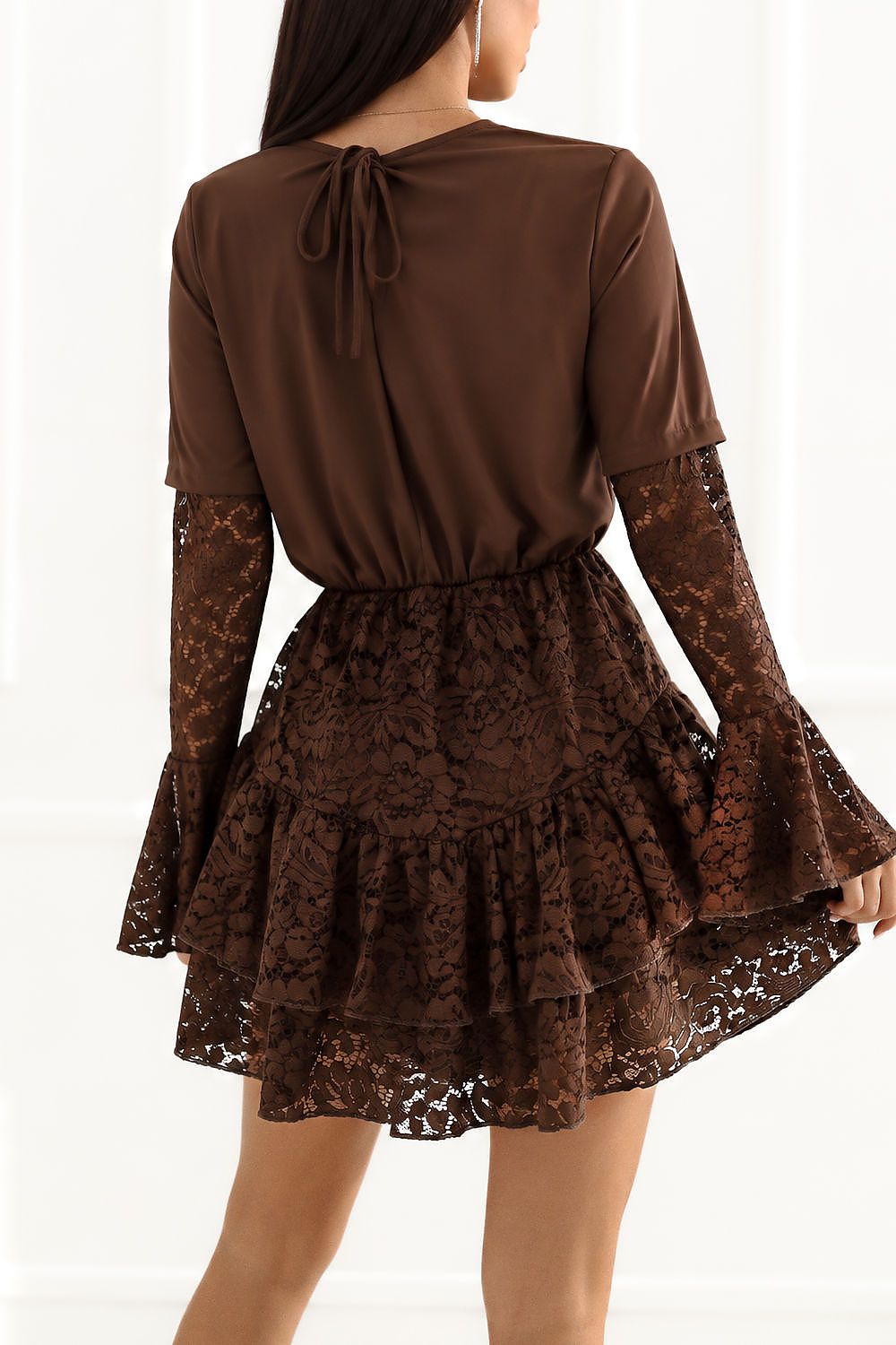 A woman shown from the back wearing a brown long-sleeve top and ruffled mini skirt with lace sleeves and hem, photographed against a bright white indoor background.