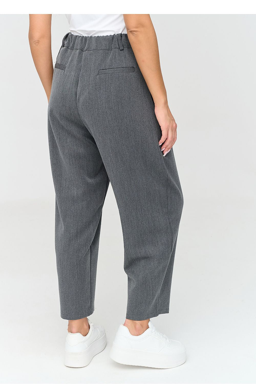 A person shown from the back wearing dark gray cropped trousers with an elastic waistband, side pockets, and a relaxed straight-leg fit, paired with white sneakers against a light gray studio background.