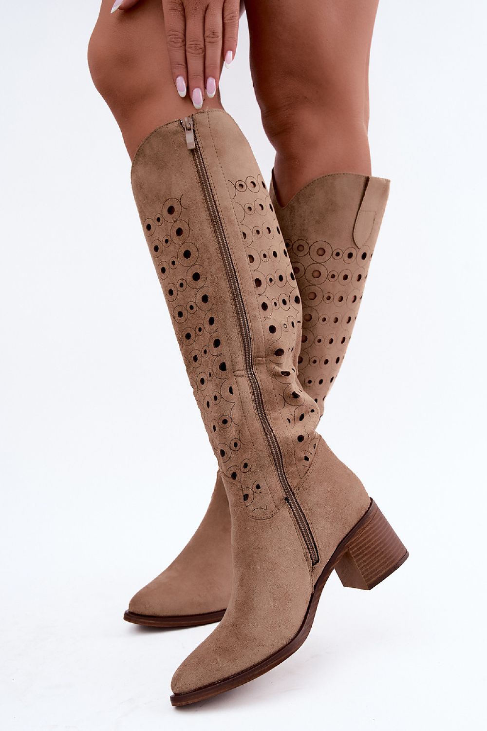 A pair of knee-high taupe suede boots with decorative side cutouts and a side zipper, shown on a model against a white background.