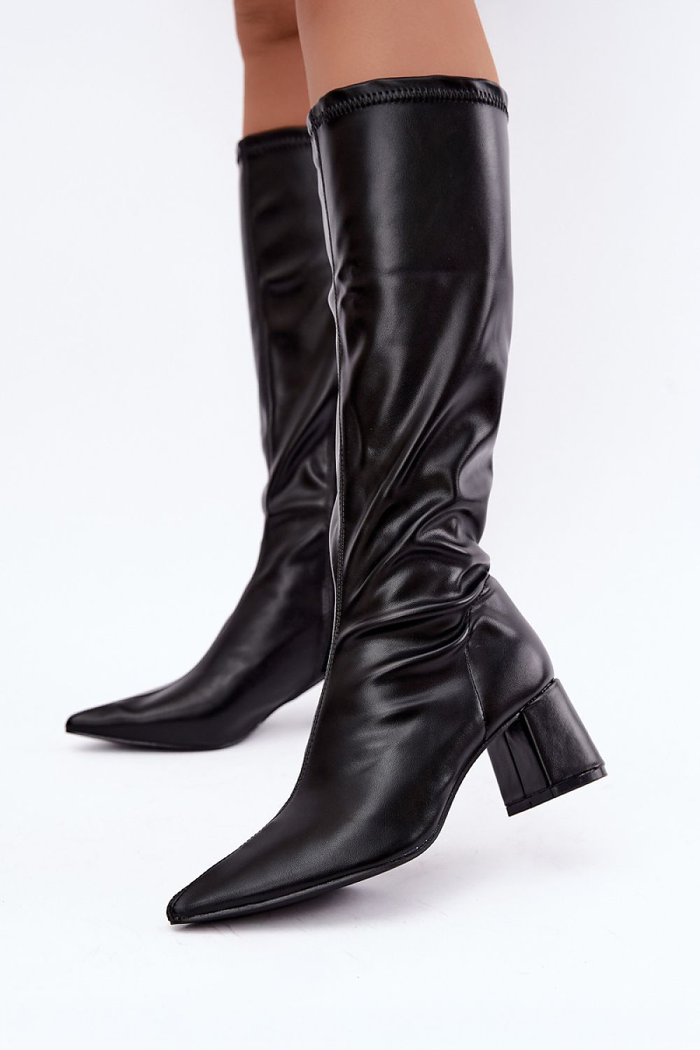 A pair of black leather knee-high boots with pointed toes and block heels, shown on a model's legs against a plain white studio background.