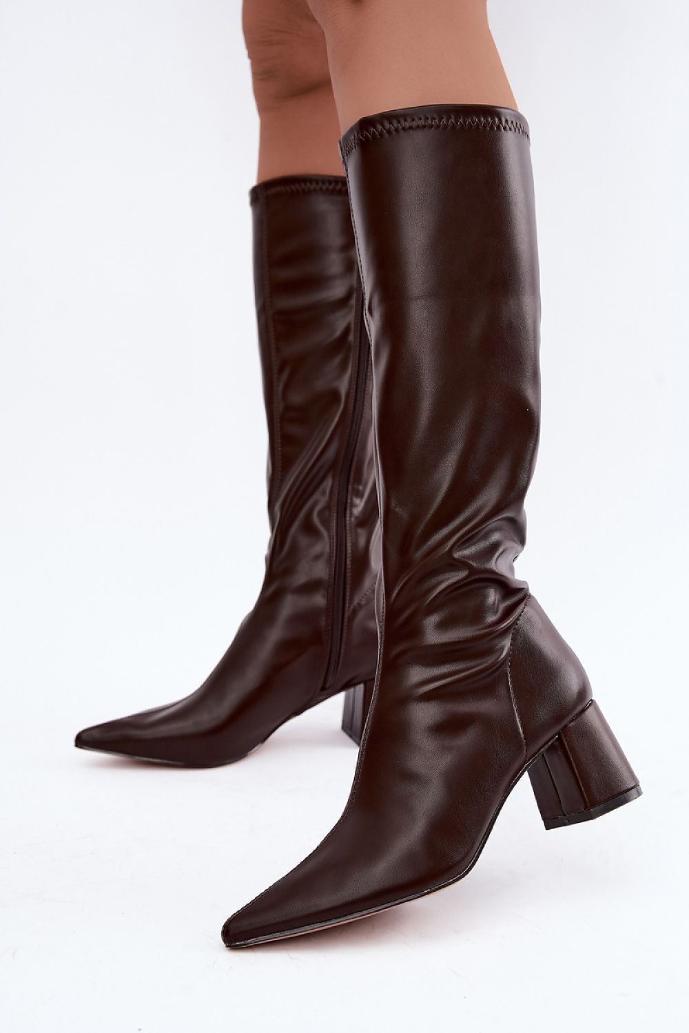 A pair of dark brown leather knee-high boots with pointed toes and block heels, shown on a model's feet against a plain white background.