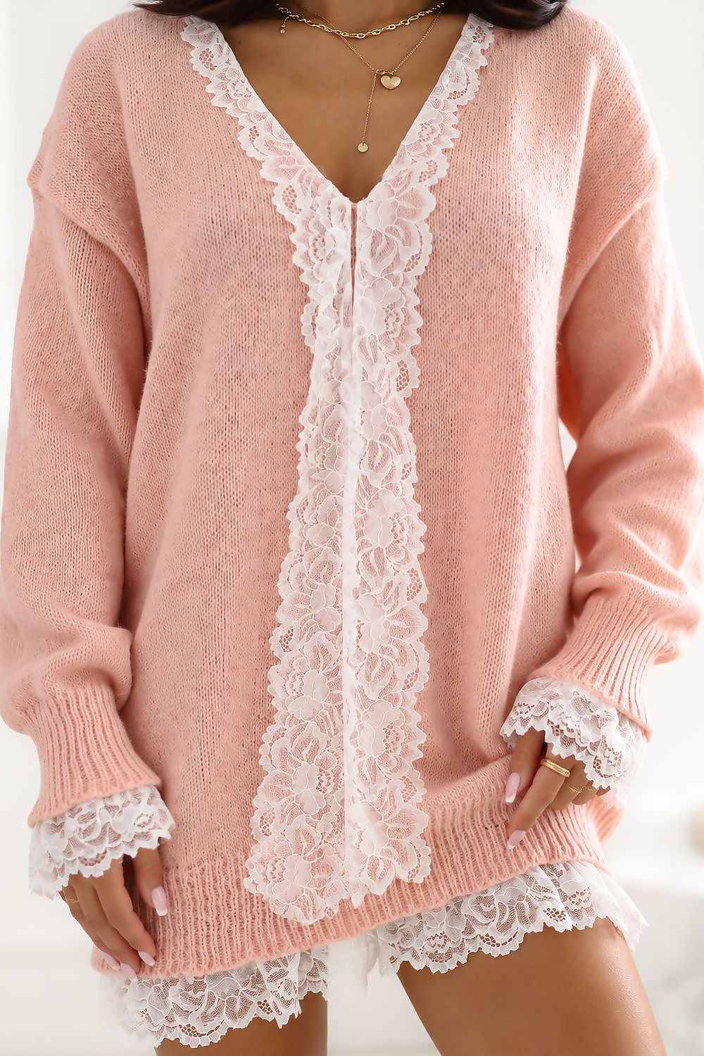 A woman wearing a pink knit cardigan sweater with white lace trim along the front opening, cuffs, and hem.