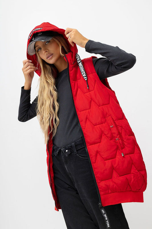 A woman models a bright red hooded puffer vest over a black long-sleeve shirt and black jeans against a plain light gray studio background.