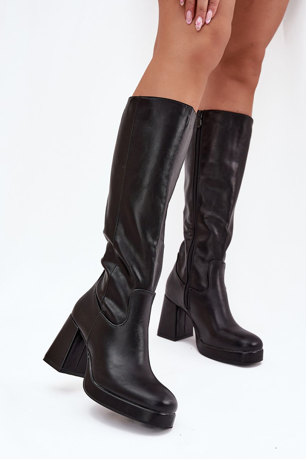A pair of black knee-high boots with chunky block heels, shown on a model's feet against a plain white background.