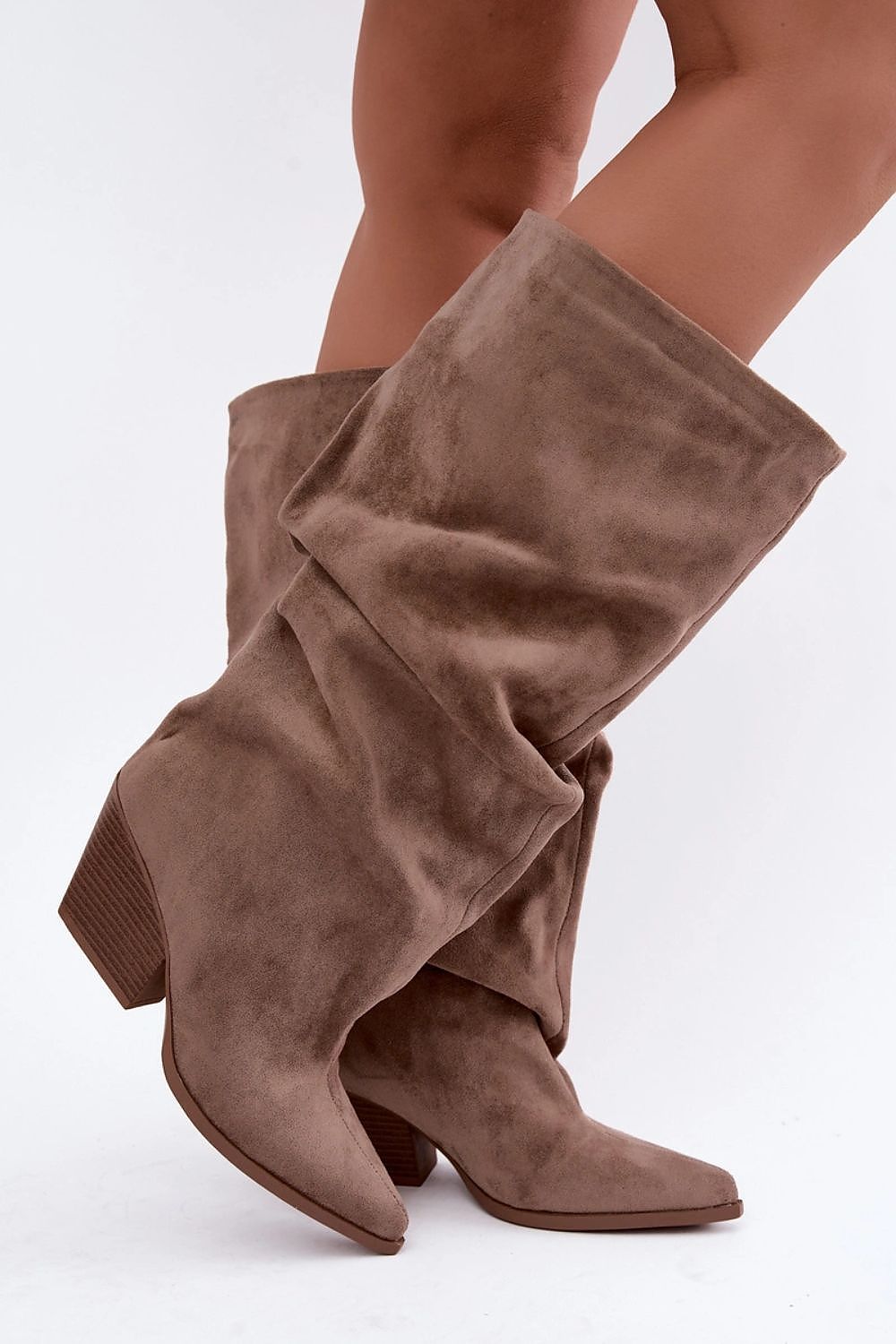 A pair of mid-calf brown suede boots with a draped, slouchy design and low block heels, shown on a model's legs against a white studio background.