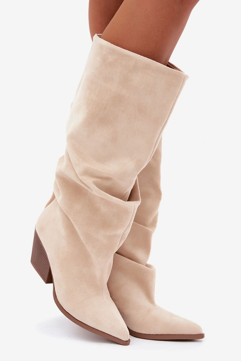 A pair of knee-high beige suede boots with a pointed toe and low block heel, shown on a model's feet against a light gray background.