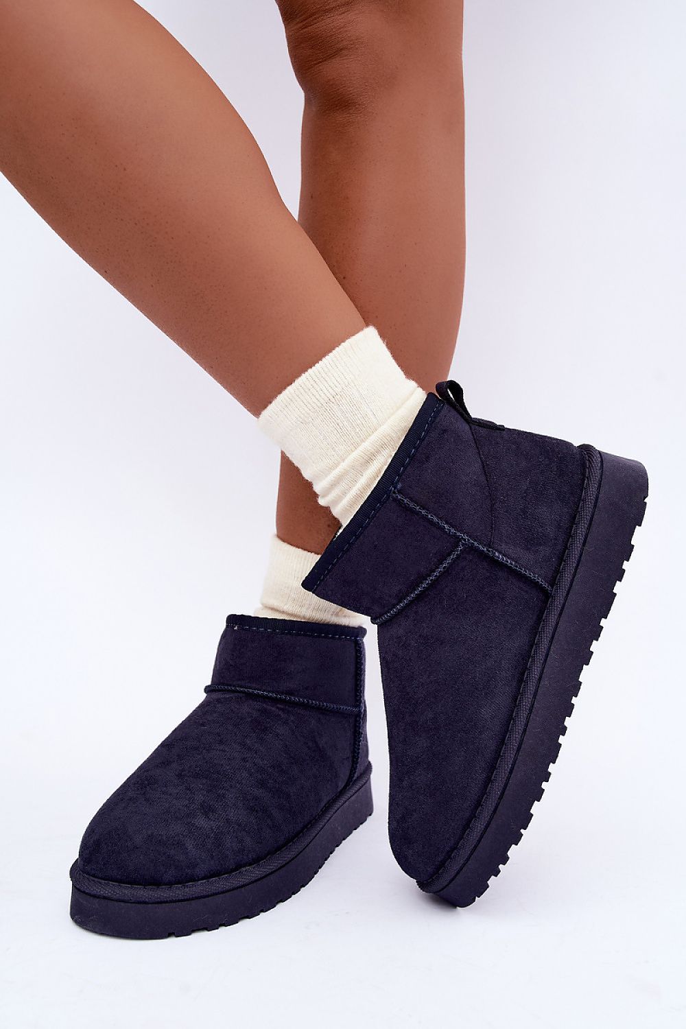 A person wearing navy blue suede ankle boots with cream ribbed socks, shown from the calves down against a clean white studio background.