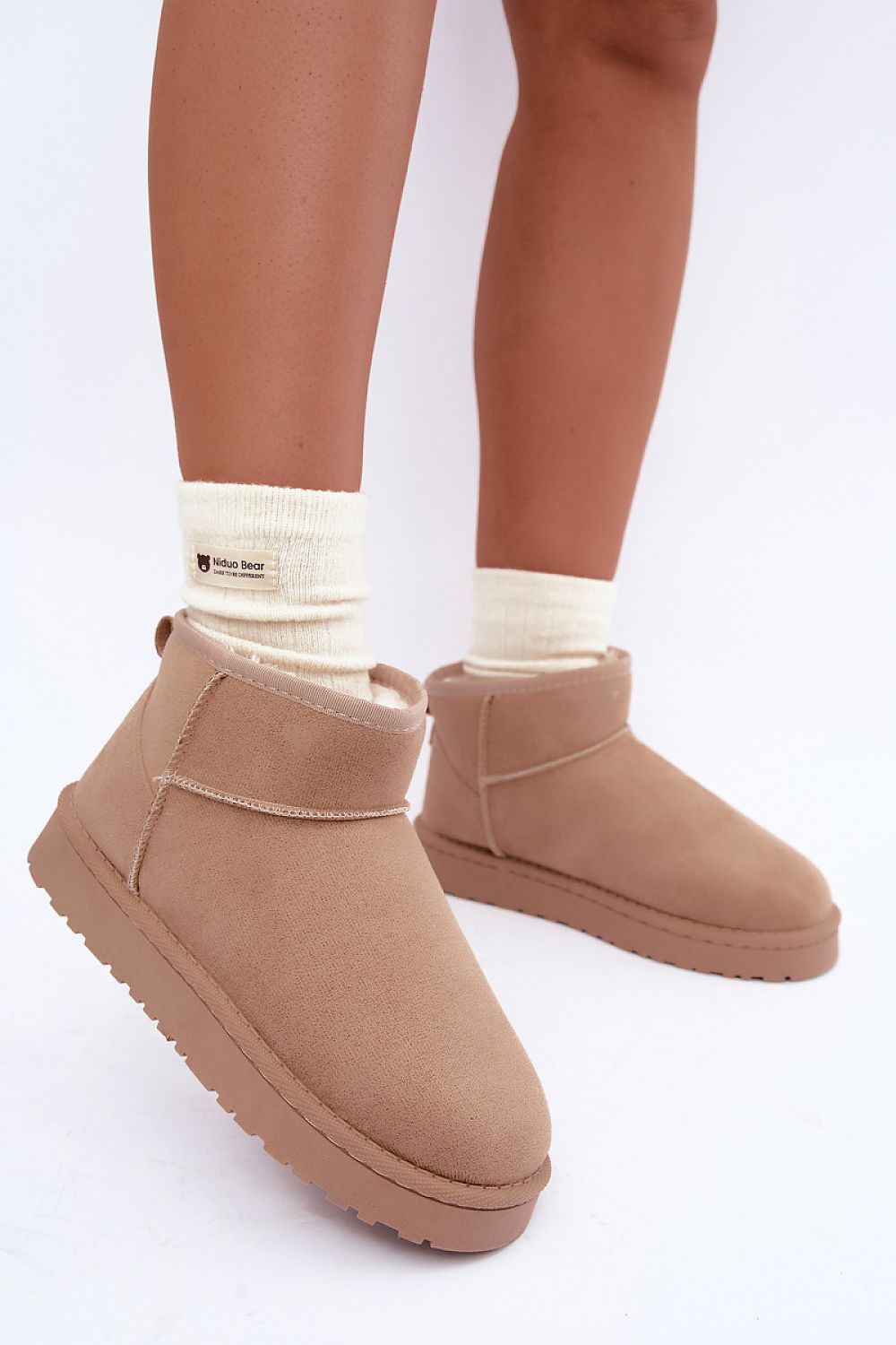 A person wearing tan suede-like ankle boots with cream socks, shown from the calves down against a clean white studio background.