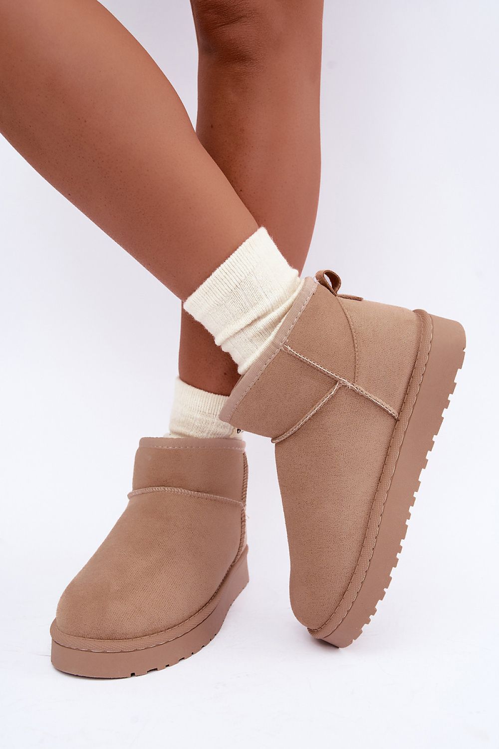 A pair of taupe suede ankle boots with platform soles, shown on a model's feet with cream ribbed socks against a white studio background.