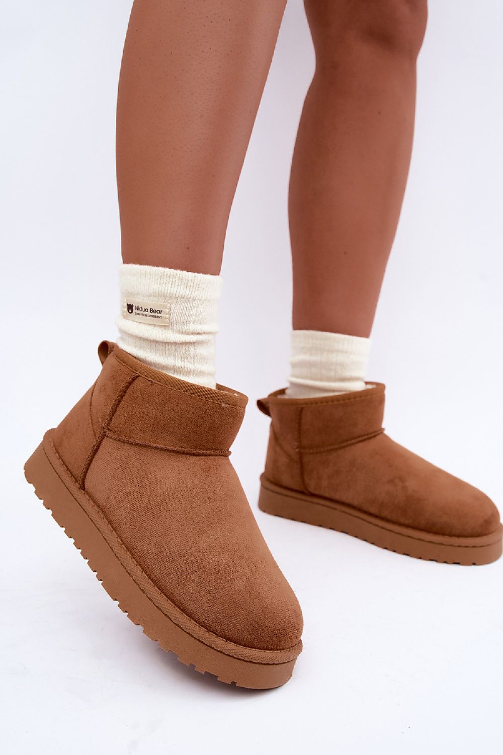 A person wearing brown suede ankle boots with thick platform soles and cream-colored crew socks, shown from the calves down against a plain white studio background.
