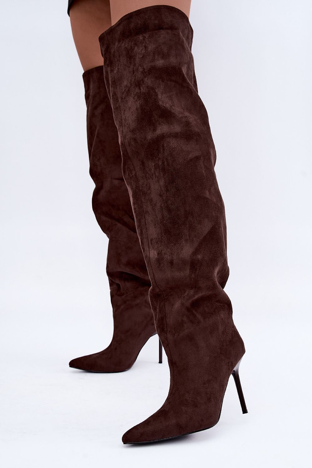 A pair of dark brown suede over-the-knee boots with pointed toes and slim high stiletto heels, shown on a model against a plain white studio background.