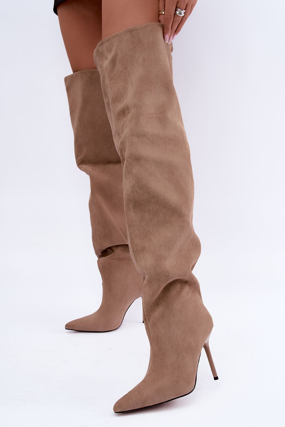 A pair of knee-high taupe suede boots with pointed toes and slim stiletto heels, shown on a model against a plain white background.