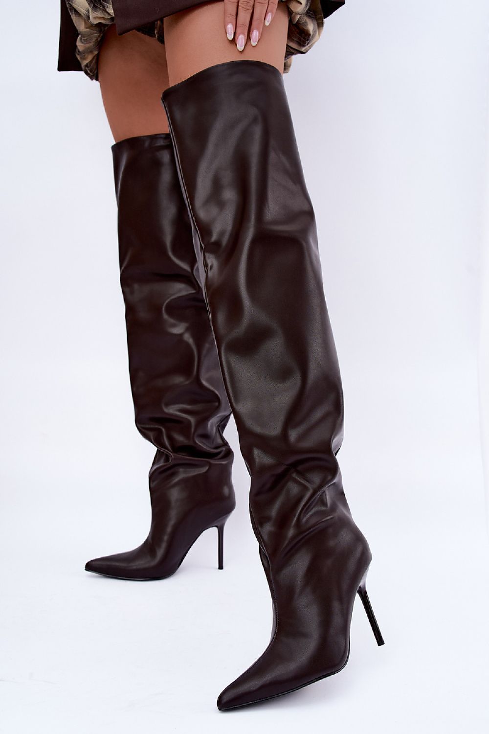 A pair of dark brown faux-leather knee-high boots with pointed toes and slim stiletto heels, shown on a model against a white studio background.