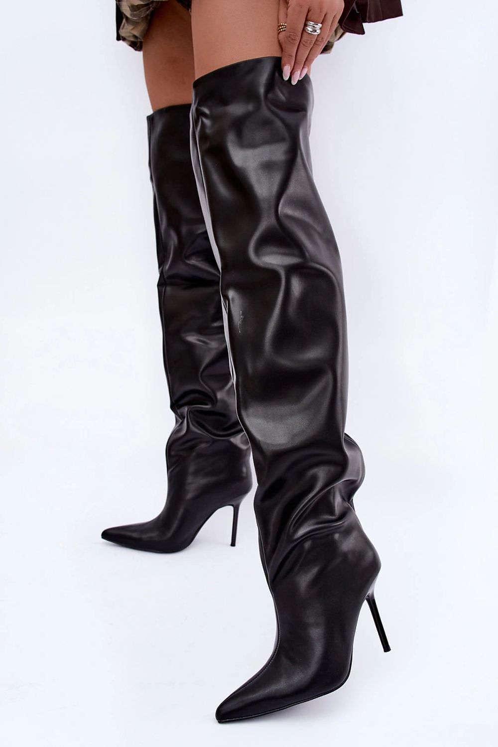 A pair of black faux-leather over-the-knee boots with pointed toes and slim stiletto heels, shown on a model against a white studio background.