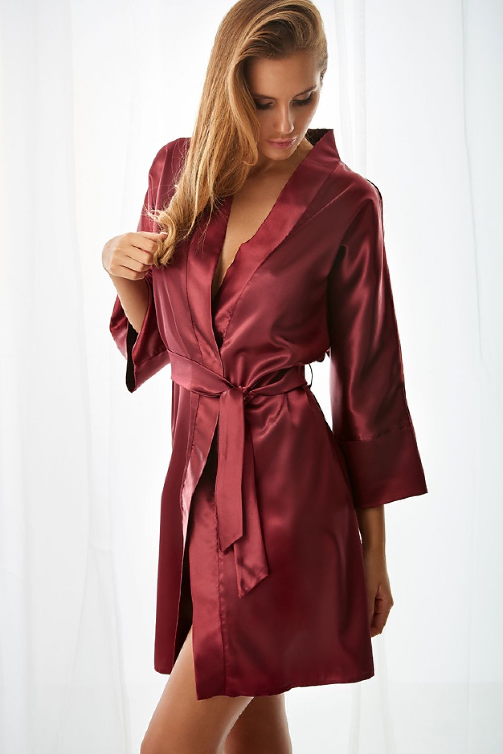 Woman wearing a burgundy satin robe holding a glass of champagne against a white background