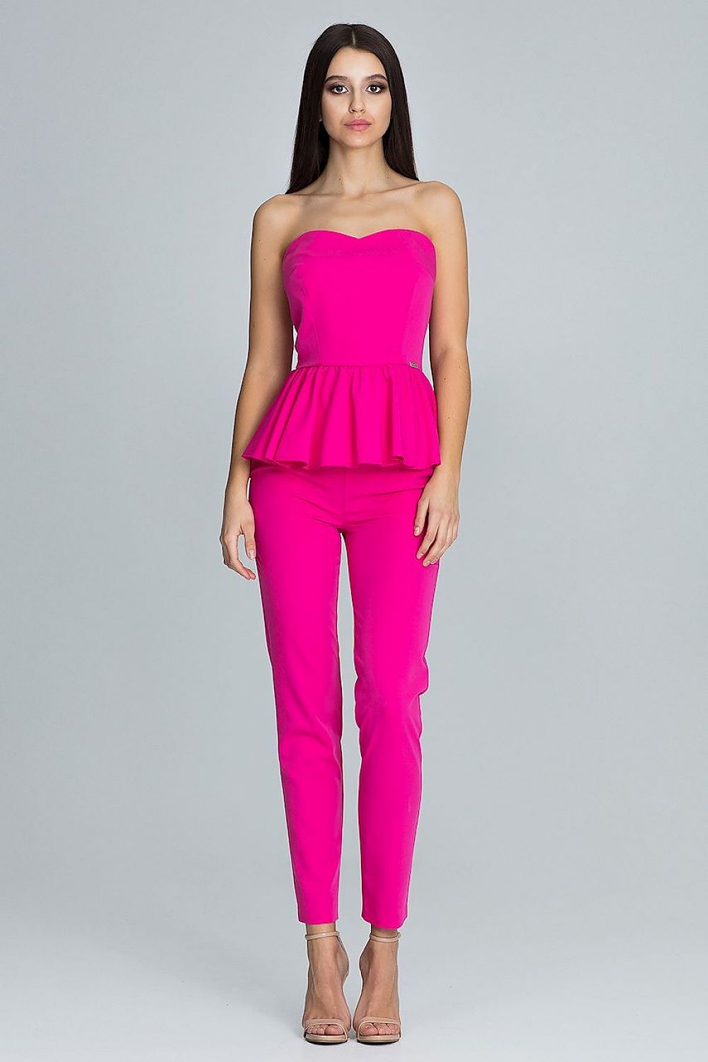 Woman wearing a bright pink strapless top and pants on a gray background