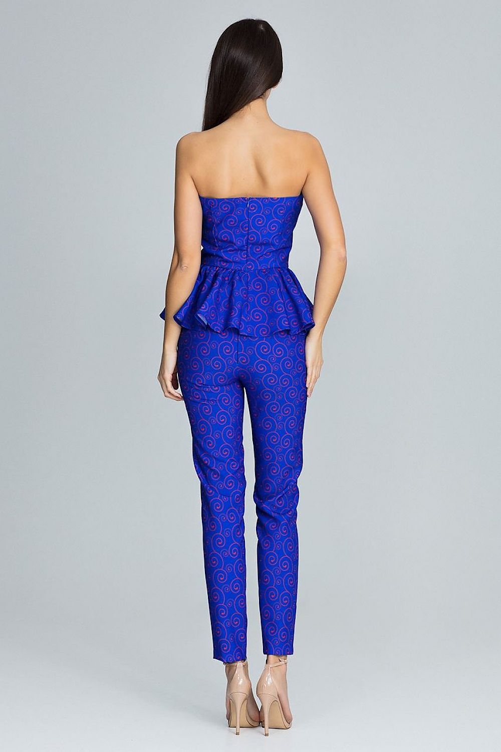Woman wearing a blue strapless jumpsuit with a pattern on a gray background