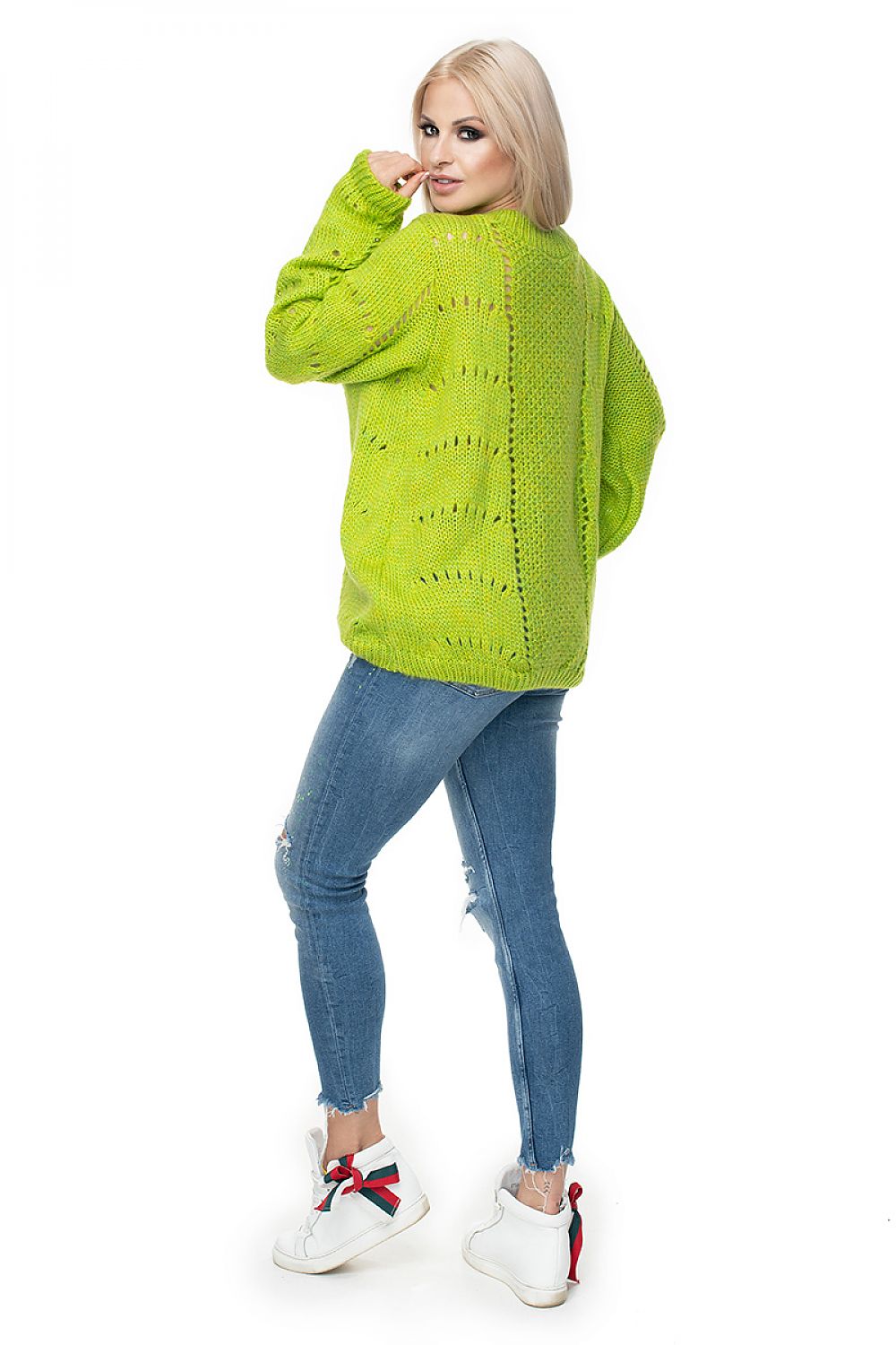 Woman wearing a bright green knitted sweater and blue jeans on a white background