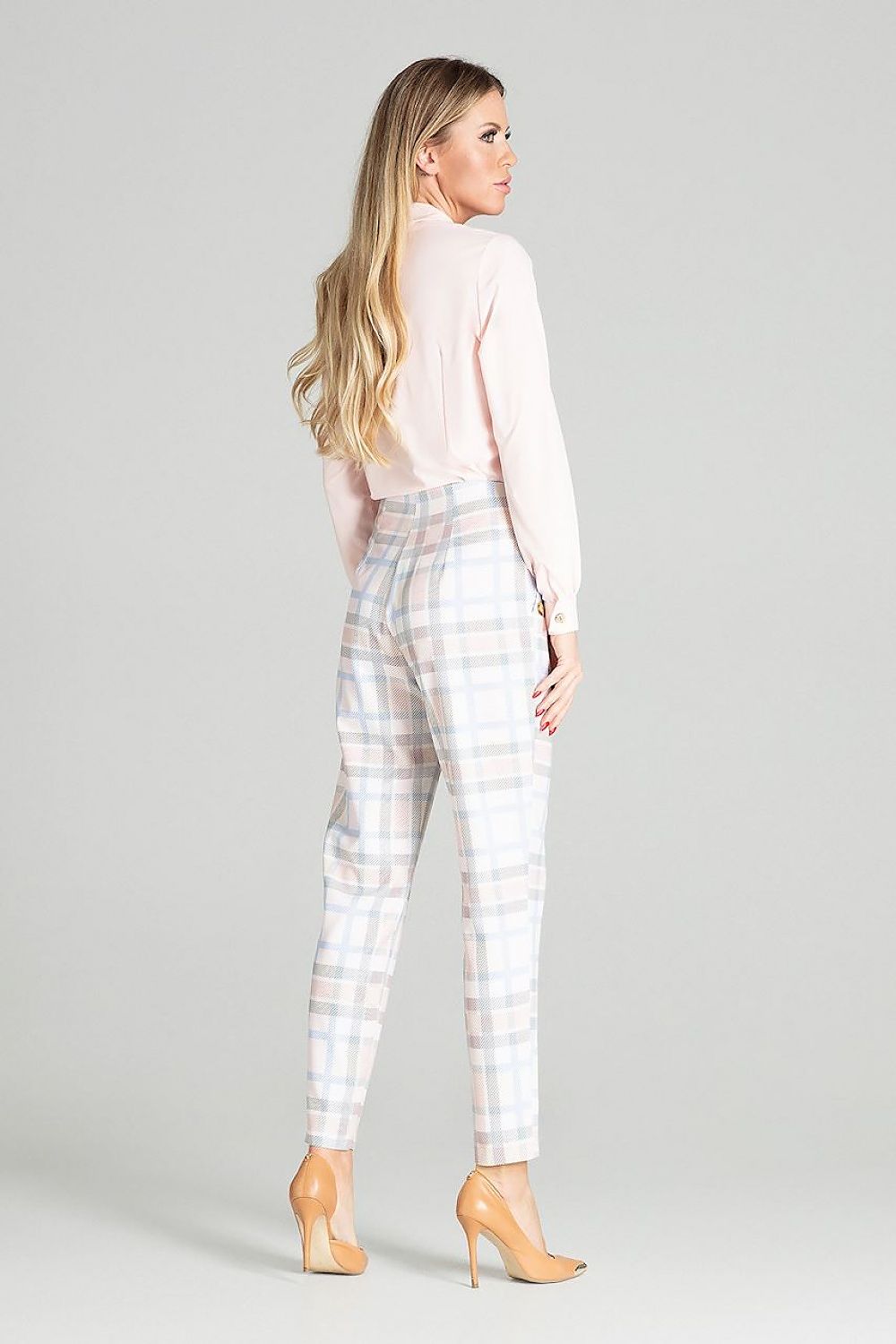 Woman wearing a light pink blouse and plaid pants on a gray background
